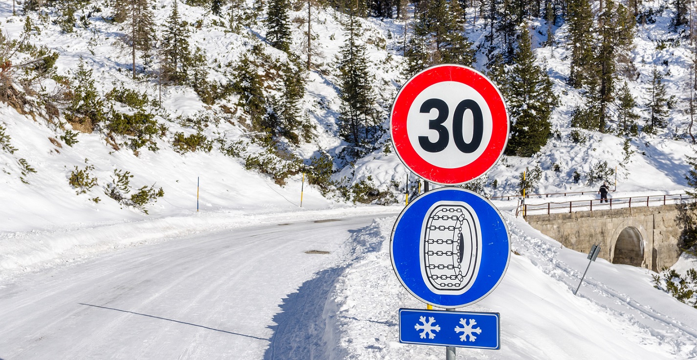 weg in winter met sneeuw met bord voor sneeuwkettingen en snelheidsbeperking 30 km/u